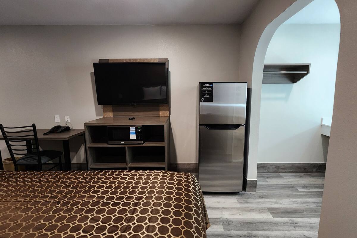 Ein Hotelzimmer mit einem Bett, einem Schreibtisch mit Stuhl, einem Flachbildfernseher, einem Kühlschrank und einer Mikrowelle.