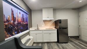 A compact kitchen with white cabinets, a stainless steel refrigerator, and a built-in air conditioner. - Hotel Park Place (Houston)