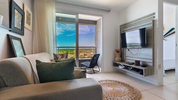 A modern living room with a large TV, a sofa, a chair, and a balcony with a view. - CJC Short Stay Blue Ocean (Natal)