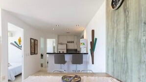 A modern kitchen with white cabinets, a refrigerator, and a dining area with a table set for two. - CJC Short Stay Blue Ocean (Natal)