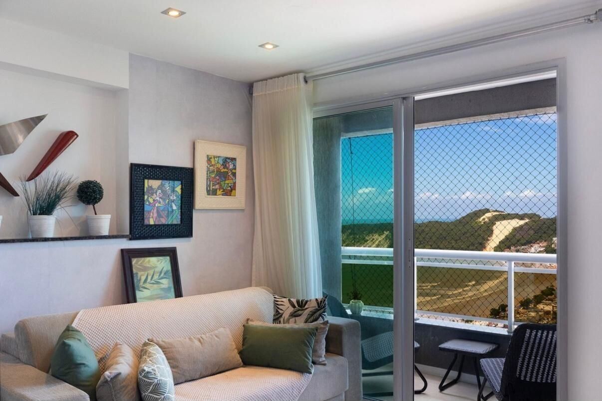 A modern living room with a sofa, a dining table, and chairs. There is a large window with a view of a landscape.