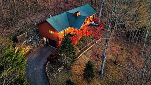 Una baita di legno a due piani con tetto verde, un portico coperto e un garage.