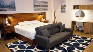Een slaapkamer met een bed, een grijze bank, een bureau met stoel, en een spiegel.