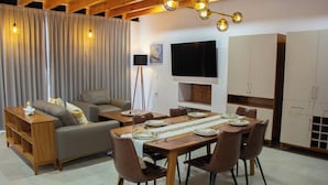 Een moderne woonkamer met een bank, een eettafel gedekt voor vier personen, en een televisie aan de muur.