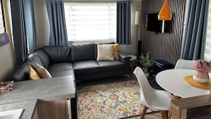 A compact living space with a sofa, dining table, chairs, and a TV. - Tranquil Caravan Retreat by the Seaside, Portseton (Prestonpans)