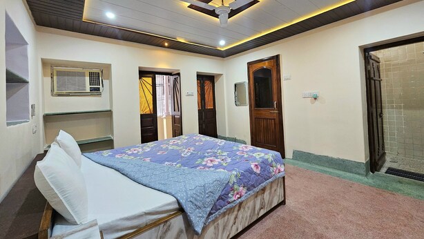 A bedroom with a bed, a ceiling fan, and a window with blinds. - Saraogi Homestays (Varanasi)