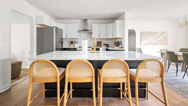 A modern kitchen with a central island, wooden chairs, and a dining area with a table and chairs.