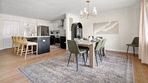 A modern kitchen with white cabinets, a central island, and a dining area with a wooden table and chairs.