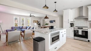 Una cocina moderna con armarios blancos, una isla central, electrodomésticos de acero inoxidable e iluminación colgante.