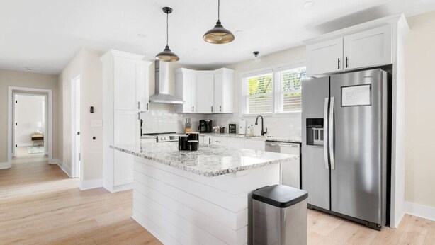 Una cocina moderna con armarios blancos, encimera de granito, electrodomésticos de acero inoxidable e iluminación colgante.