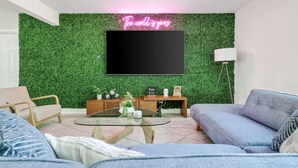 Una sala de estar con pared verde, televisor de pantalla plana, sofá, mesa de centro y lámpara.