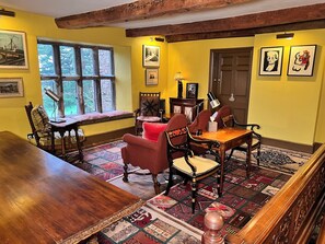 A dining room with a wooden table, chairs, and a bench. There are framed pictures on the walls and a window with a view of trees. - Uplands (Ledbury)