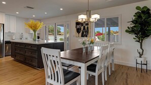 A modern kitchen with white cabinets, a wooden dining table, and chairs. There is a vase with flowers on the table, and a plant next to the window. - ☆Scottsdale Serenity☆ with big pool, putting green and HOT TUB (Scottsdale)