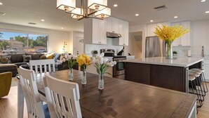 A modern kitchen with a central island, white cabinetry, stainless steel appliances, and a dining area with a wooden table and white chairs. - ☆Scottsdale Serenity☆ with big pool, putting green and HOT TUB (Scottsdale)