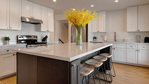 A modern kitchen with white cabinetry, a stainless steel stove, a large island with bar stools, and a vase of yellow flowers. - ☆Scottsdale Serenity☆ with big pool, putting green and HOT TUB (Scottsdale)