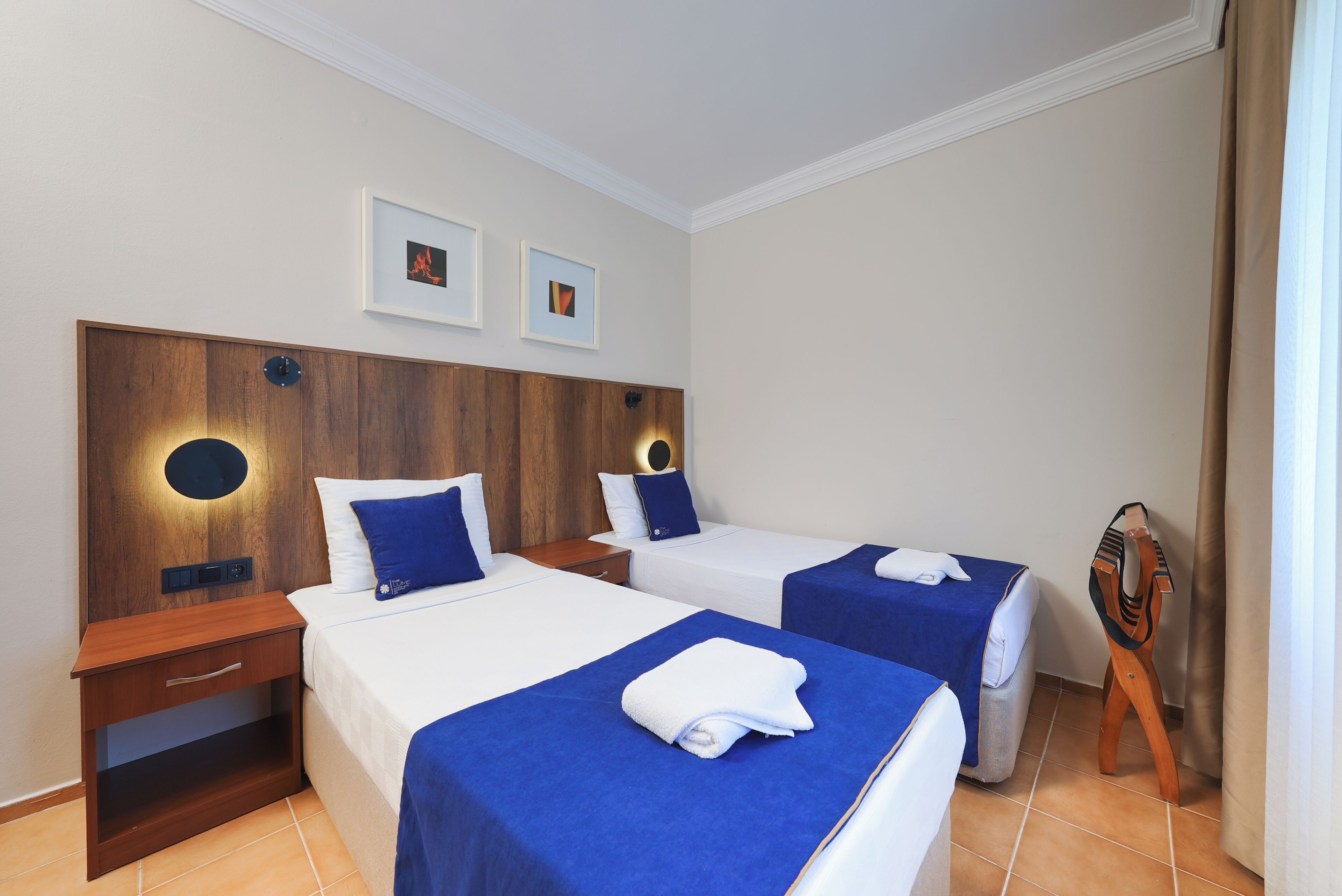 A hotel room with two beds, a wooden headboard, a nightstand, a wall-mounted lamp, and a small wooden sculpture.