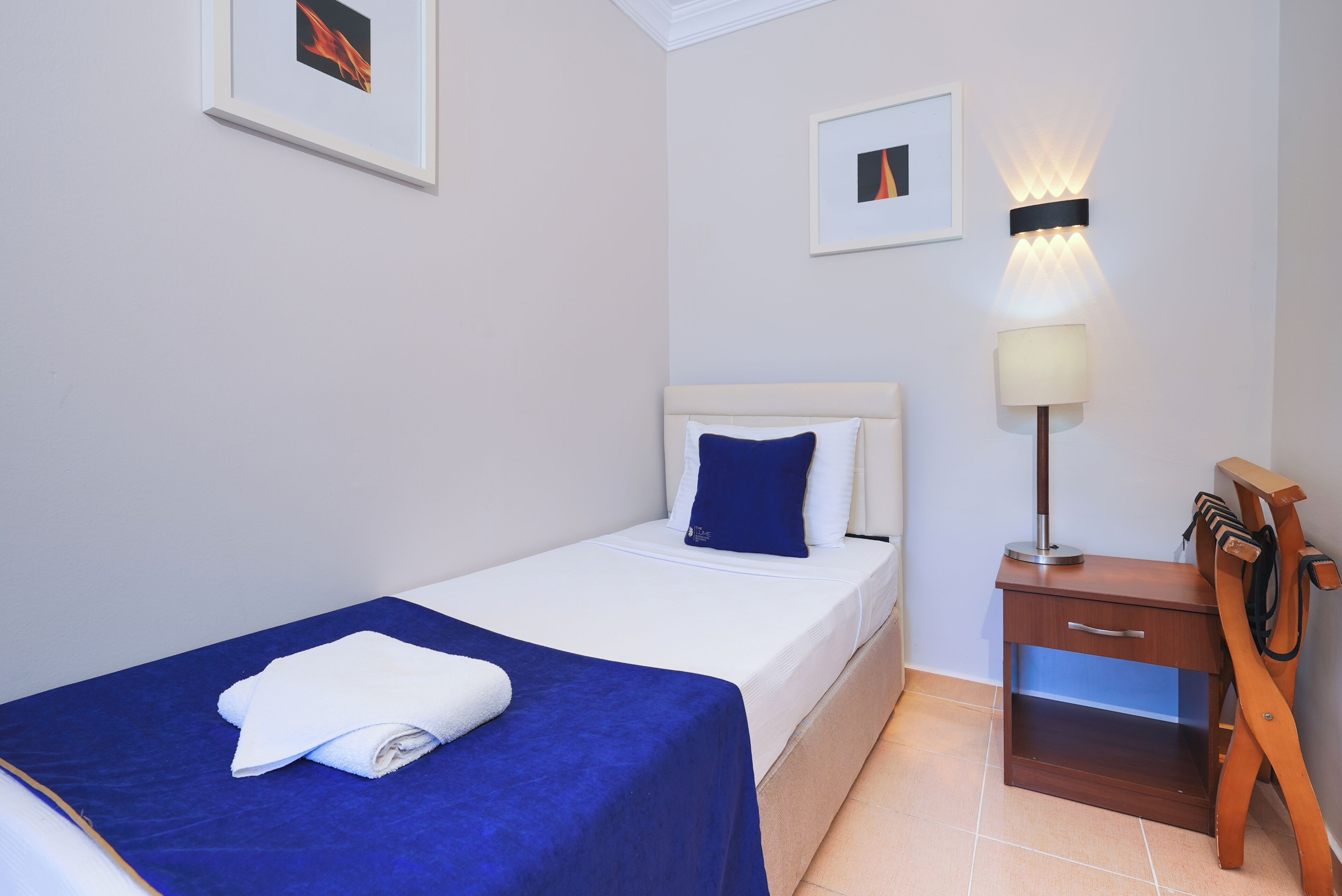 A hotel room with a bed, a bedside table with a lamp, and a wall-mounted TV.