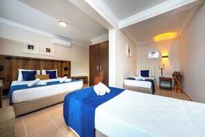 Habitación de hotel con dos camas, un armario de madera, una mesita de noche, una lámpara y un aplique de pared.