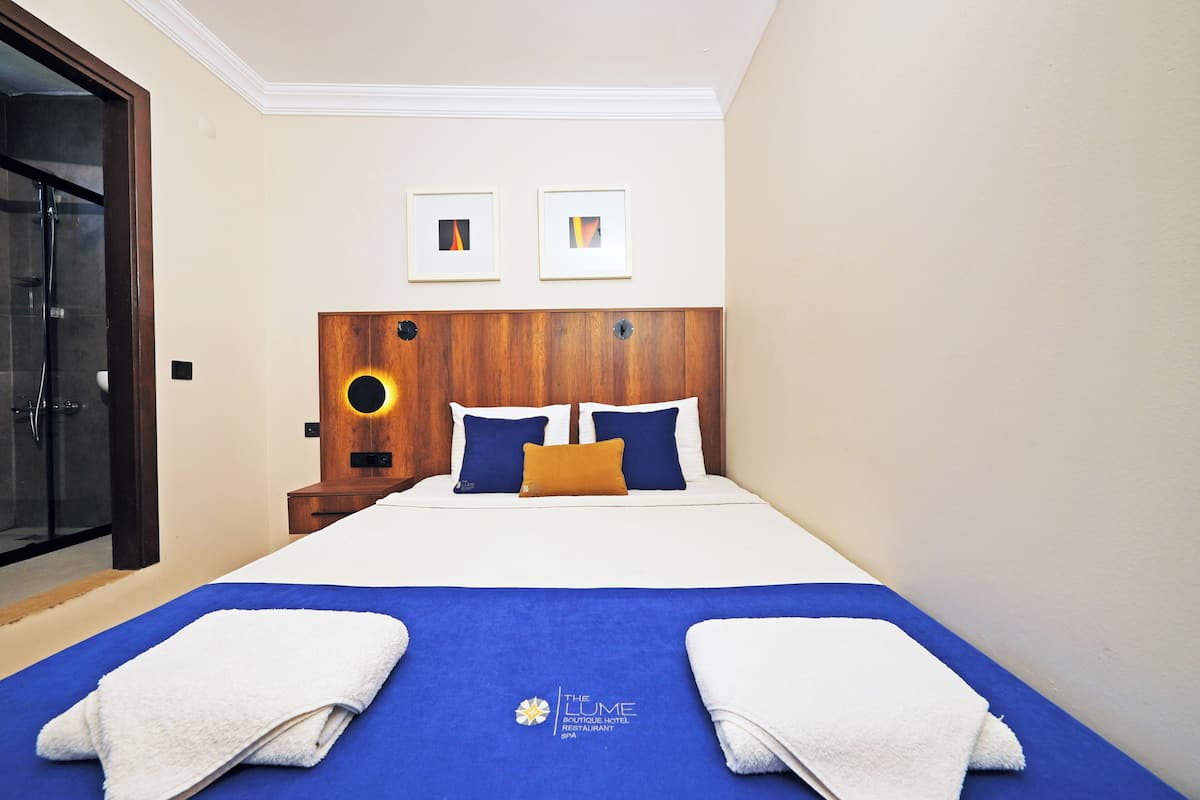 Habitación de hotel con una cama, dos cuadros en la pared, cabecera de madera y colcha azul.