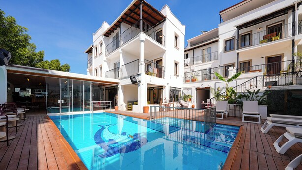 A pool area with a wooden deck, a glass-enclosed bar, and a multi-story building with balconies. - The Lume Boutique Hotel & Restaurant & Spa (Bodrum)