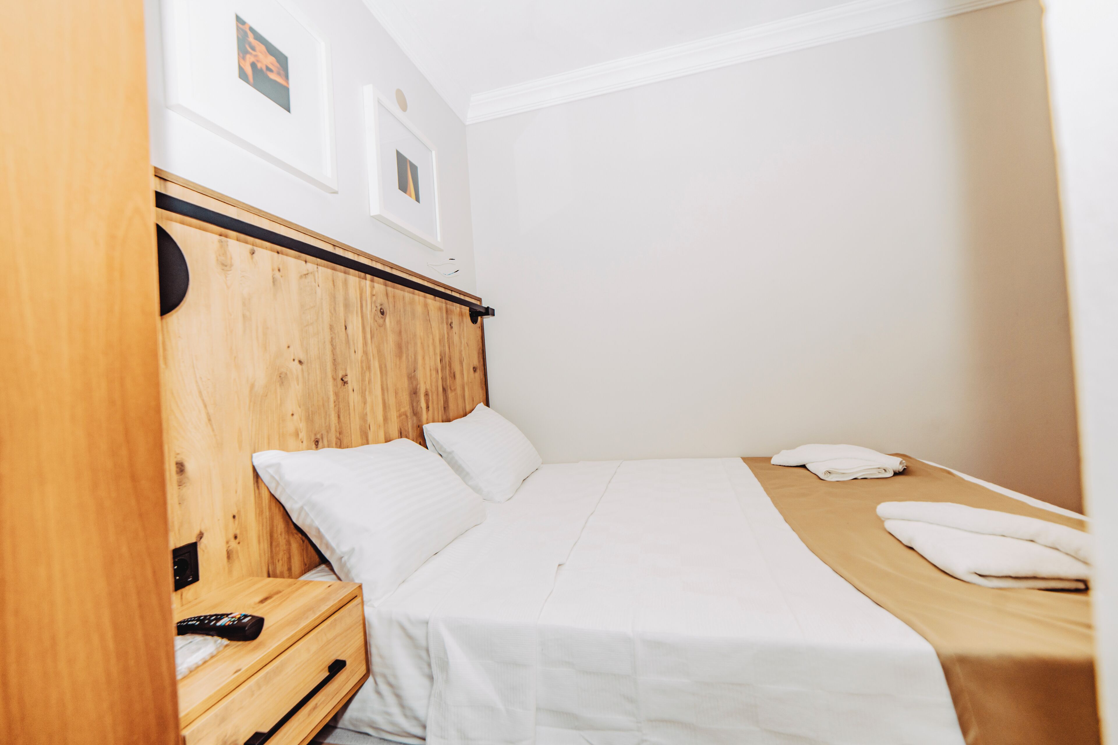 A single bed with a wooden headboard, white bedding, and a wooden nightstand with a remote control.