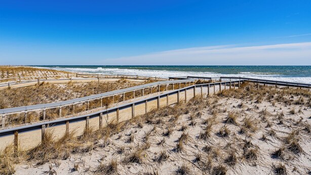 Una spiaggia con una passerella di legno e dune sabbiose.