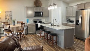 A modern kitchen with grey cabinets, stainless steel appliances, a central island with stools, and a dining area with a table and chairs.