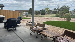 An outdoor patio area with a covered seating arrangement, a fire pit, and a view of a residential neighborhood.
