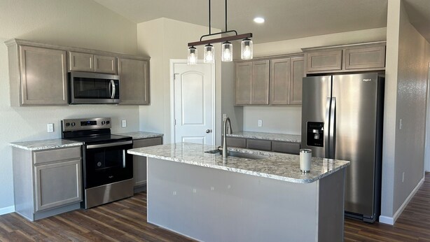 A modern kitchen with stainless steel appliances, a marble countertop island, and wooden flooring.