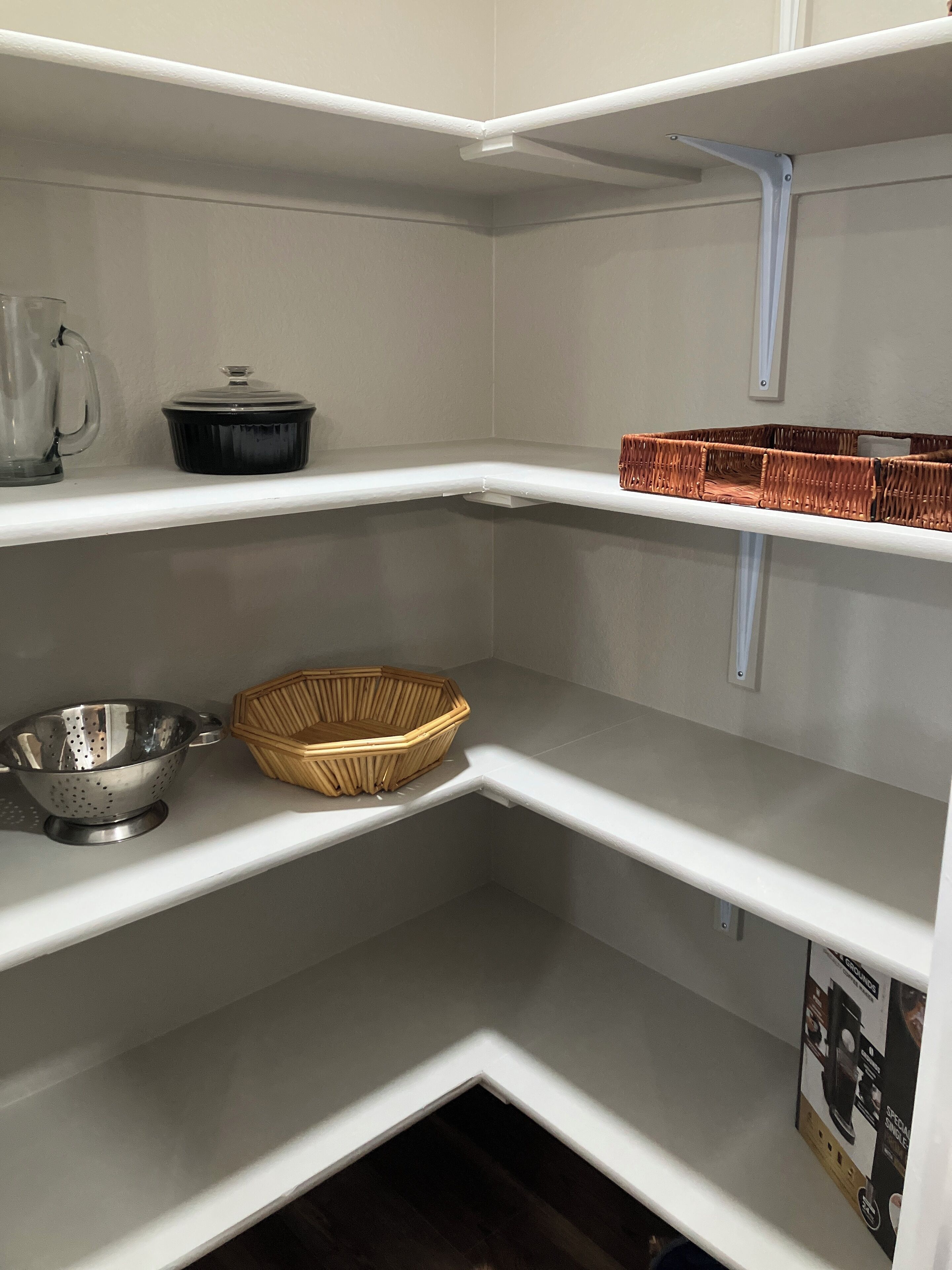 Un coin de cuisine avec des étagères blanches, une passoire, un panier en osier et une bouilloire.