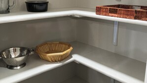 A corner of a kitchen with white shelves, a colander, a woven basket, and a kettle.