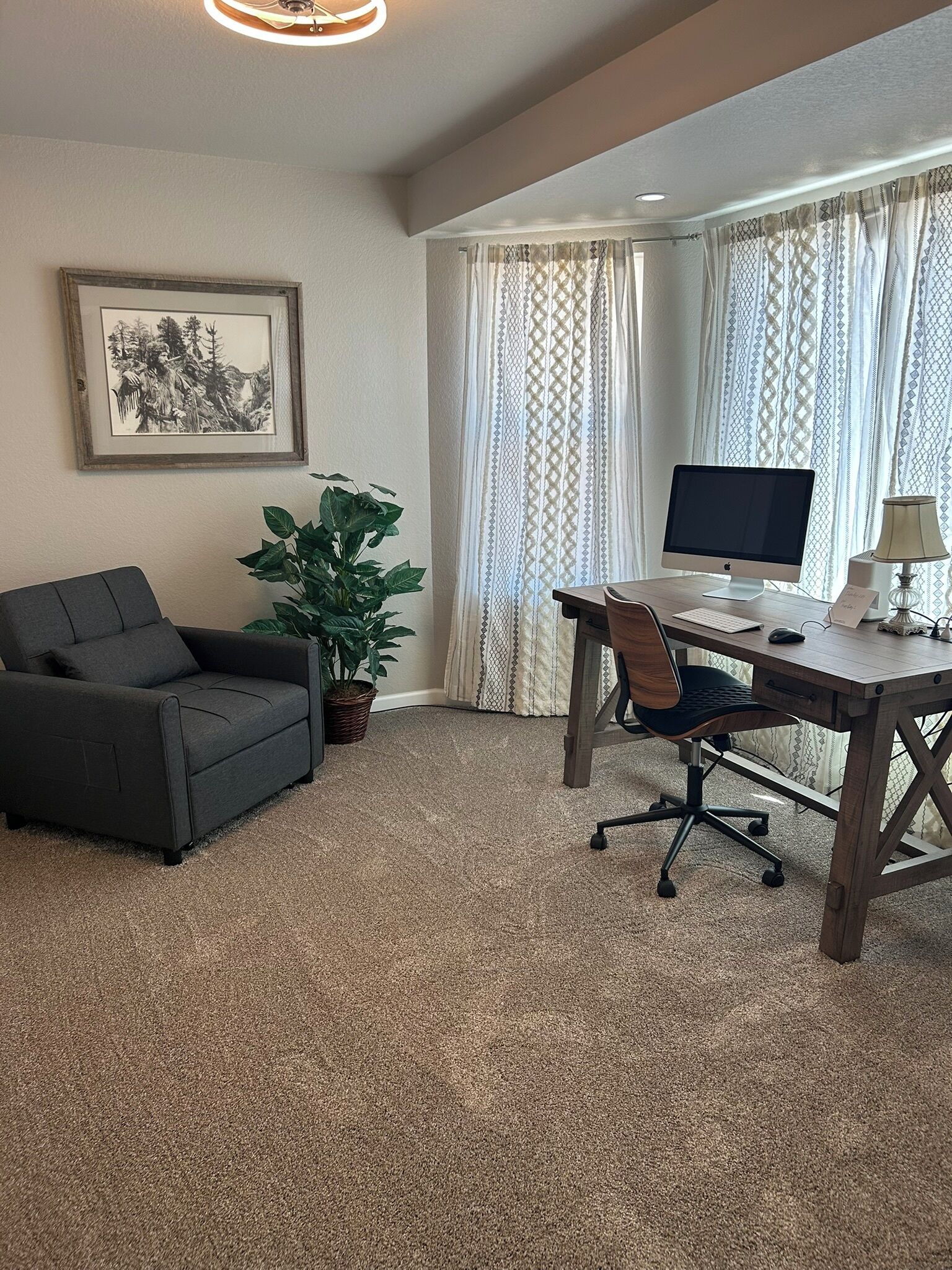 A room with a desk, computer, chair, couch, and a potted plant.