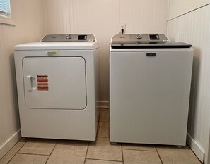 Two white Maytag appliances, a front-loading washer and a top-loading dryer, in a corner of a room with beige walls and tiled flooring.