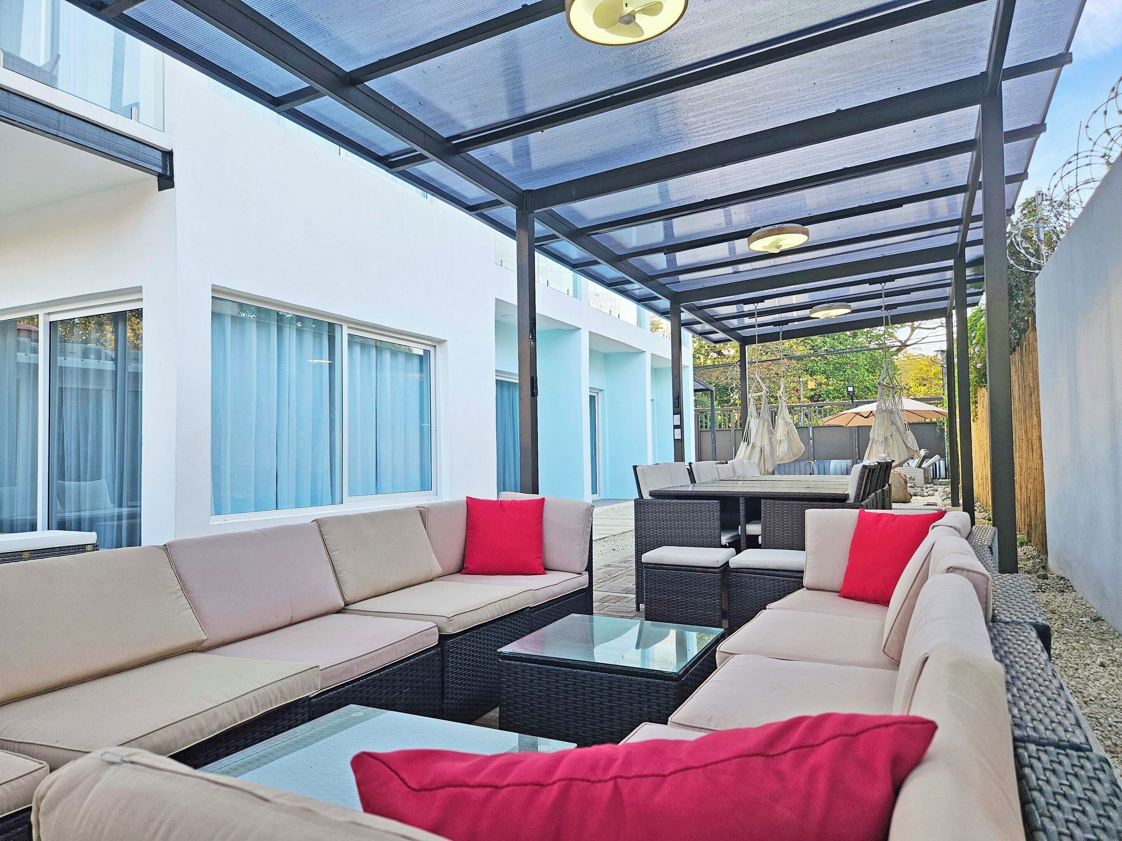 A covered outdoor seating area with sofas and a table, a glass ceiling, and a view of the backyard.