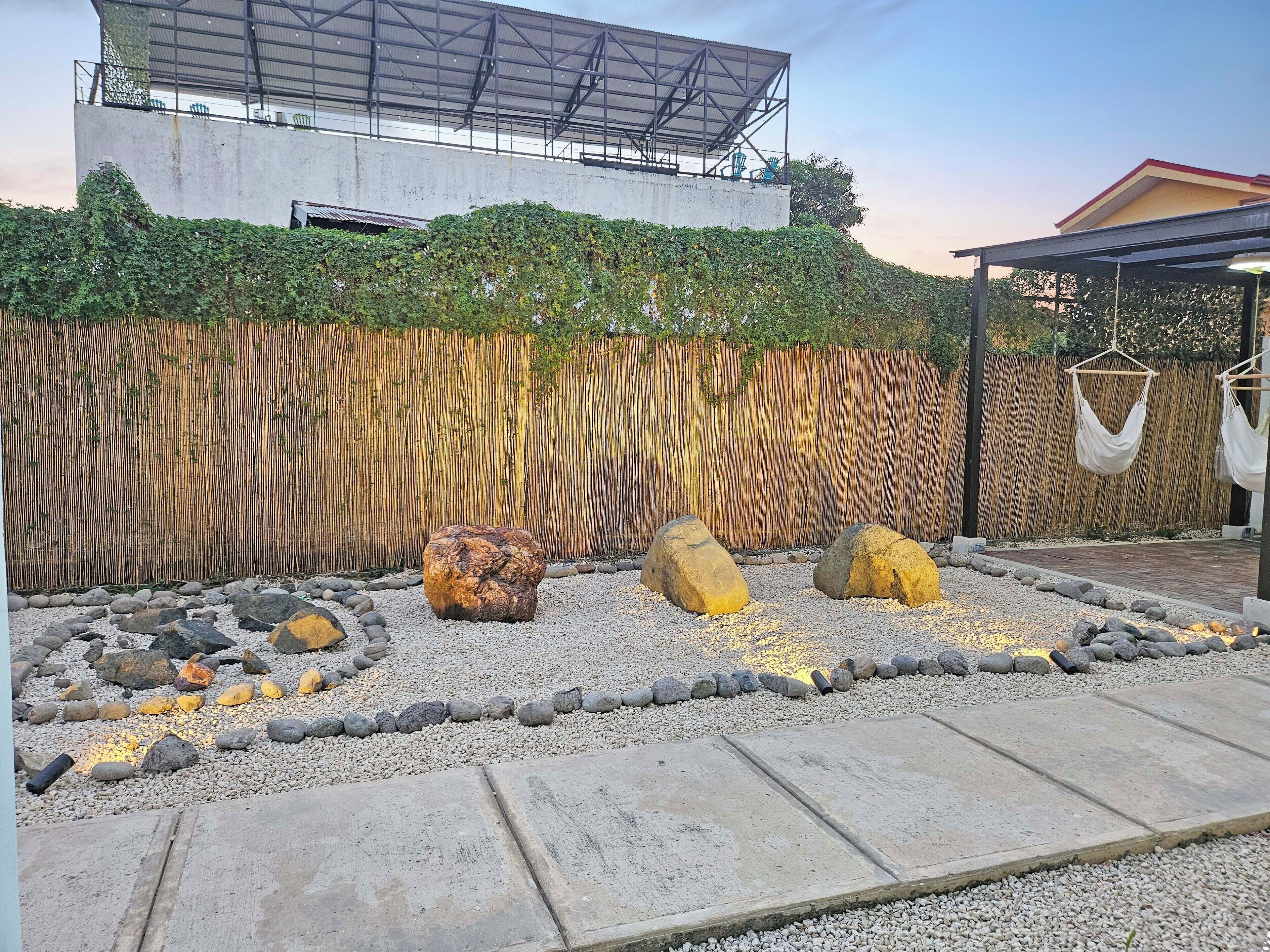 Een tuin met een bamboomschutting, grote rotsen en een betonnen pad.