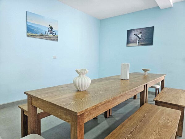 Un comedor con una mesa de madera, bancos y un jarrón. Hay dos cuadros en las paredes.