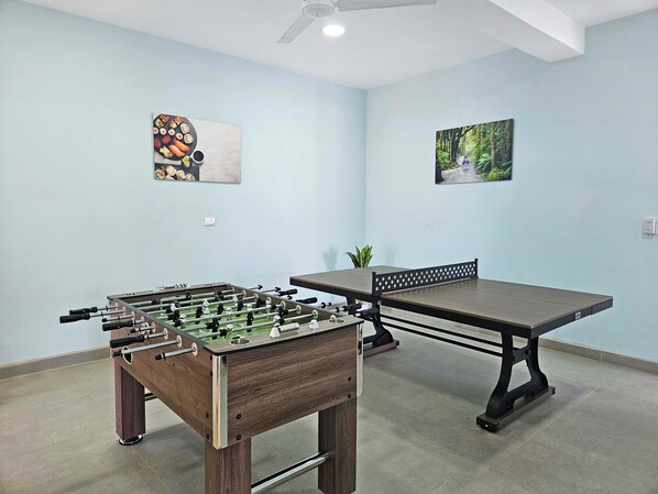 A room with a foosball table, a dining table, and two wall-mounted artworks.