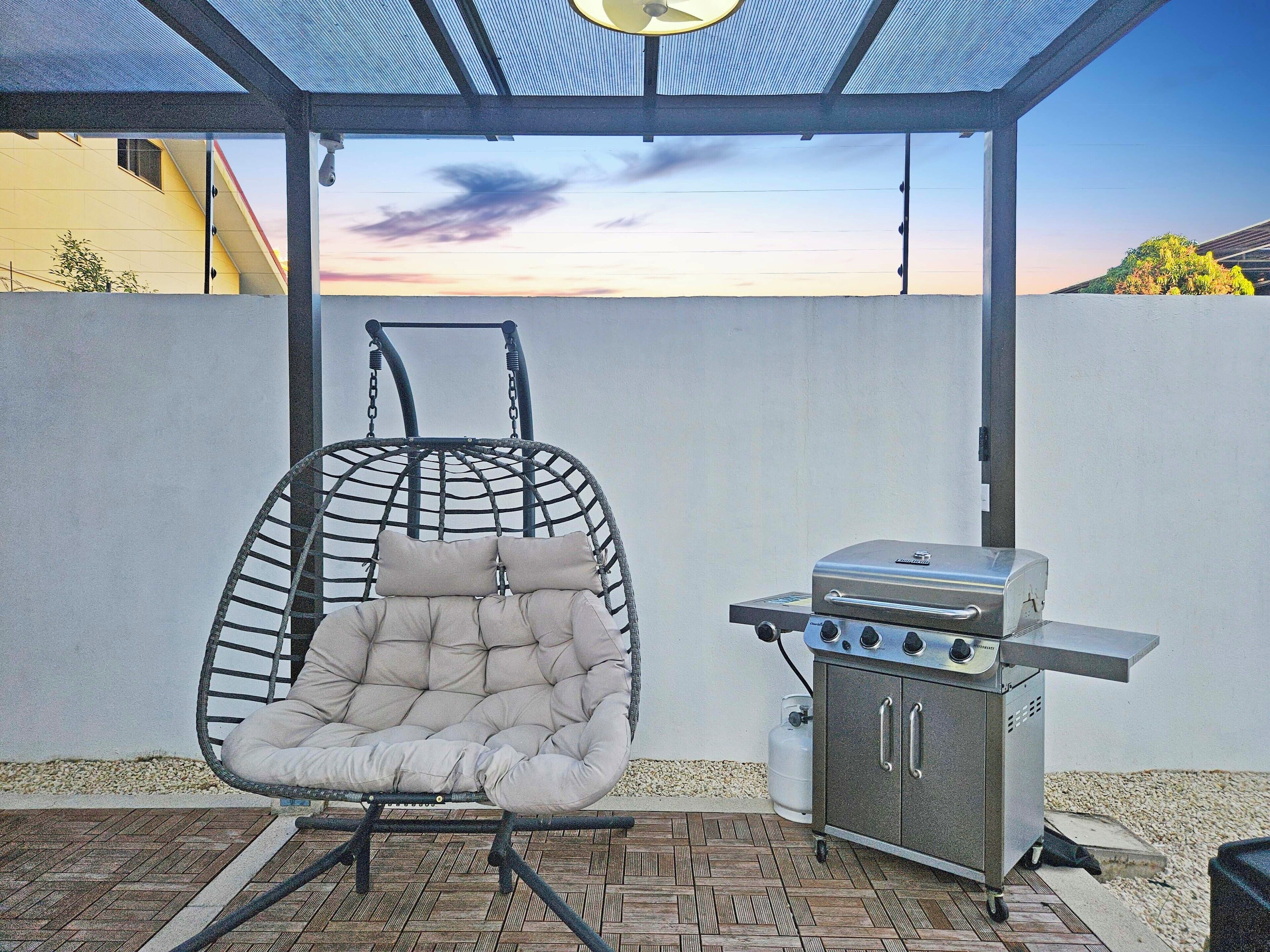 Un patio con una silla colgante y una parrilla de barbacoa.