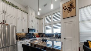 Una cocina moderna con armarios blancos, un refrigerador de acero inoxidable, una encimera de granito y taburetes negros.