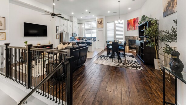 Una sala de estar moderna con un sofá de cuero negro, un comedor con mesa y sillas, una cocina con armarios blancos, y una escalera con barandillas negras.