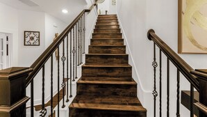 Una escalera de madera con barandilla y balaustradas oscuras, que conduce a un rellano con pared blanca y un cuadro abstracto grande.