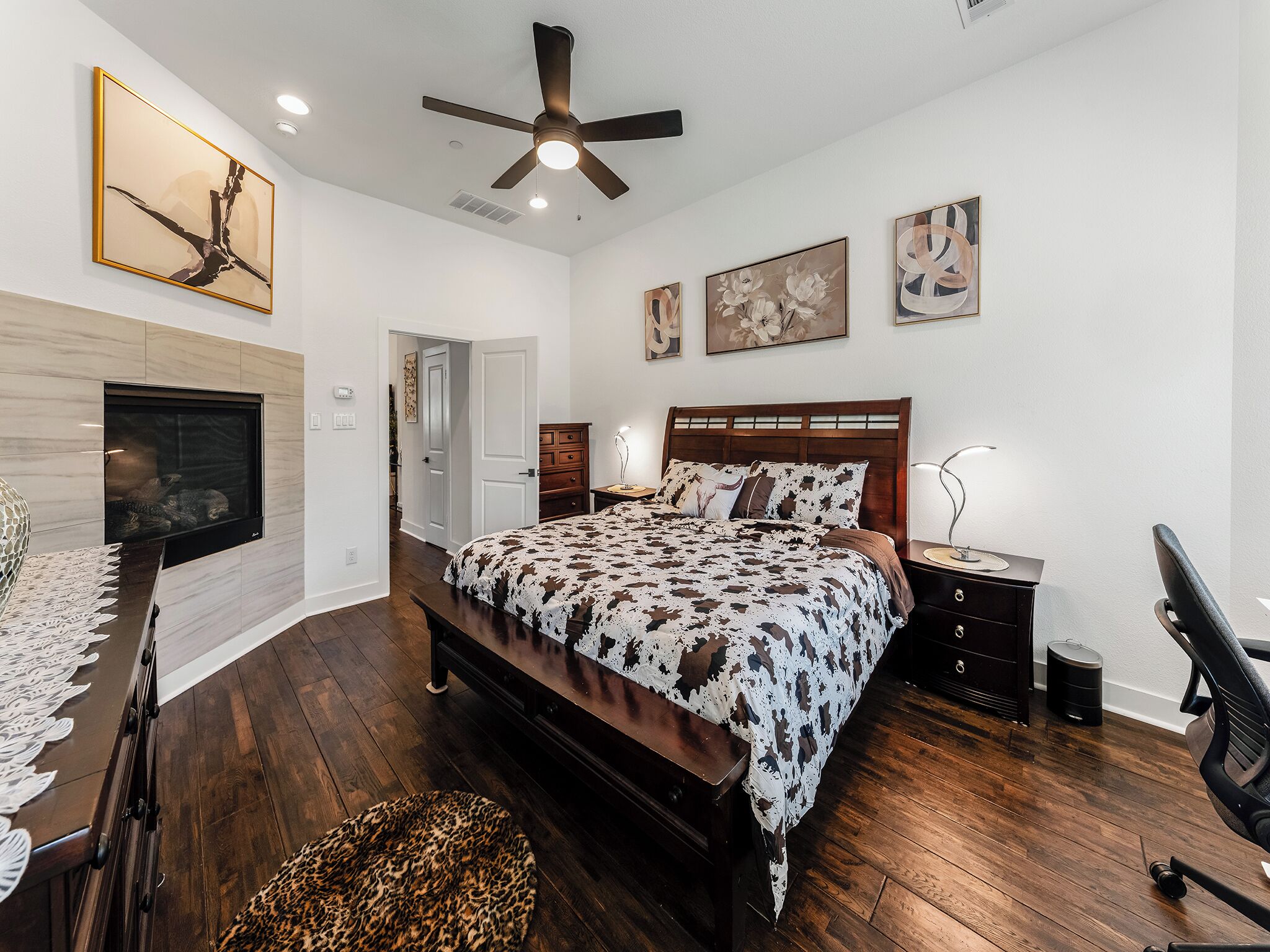A bedroom with a bed, a ceiling fan, a TV, and artwork on the walls.