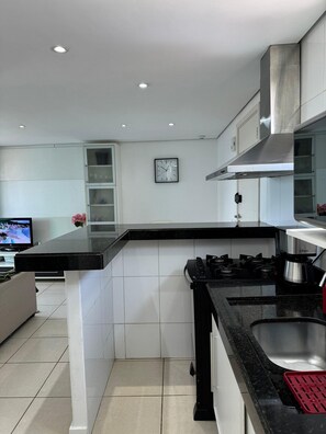A modern kitchen with a black countertop, stainless steel appliances, and a built-in oven. - CJC Short Stay D'Barcane (Natal)