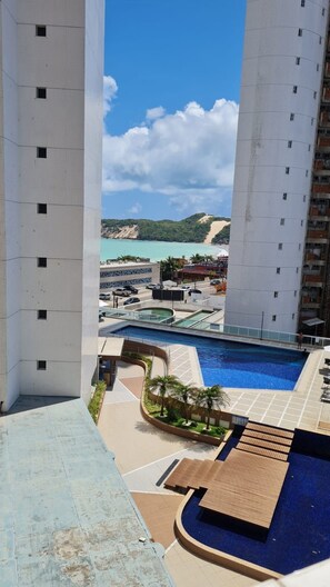 A high-rise building with a pool area, including a sun deck and lounge chairs. - CJC Short Stay D'Barcane (Natal)