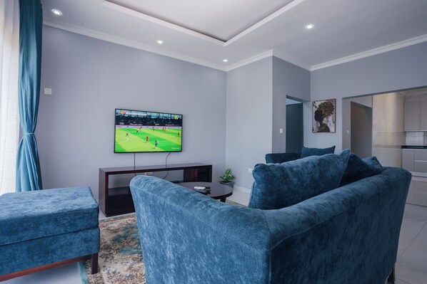 Una sala de estar moderna con un televisor de pantalla plana, muebles tapizados en azul y una planta decorativa.