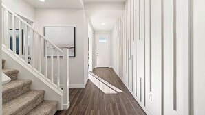 Un pasillo moderno con una escalera alfombrada, una obra de arte enmarcada en la pared y una fila de armarios a la derecha.