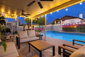 An outdoor patio area with a pool, seating, and string lights.