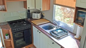Une cuisine compacte équipée d’une cuisinière à gaz, d’un grille-pain, d’un évier et d’une fenêtre donnant sur les arbres.