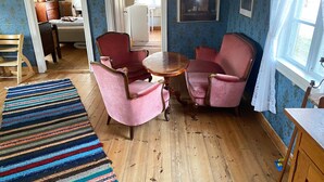 A room with a wooden floor, a striped rug, two pink armchairs, a small round table, and a window with curtains. - Charming Old Cottage in Scenic Southern Småland, Just Outside Markaryd | SE07057 (Markaryd)