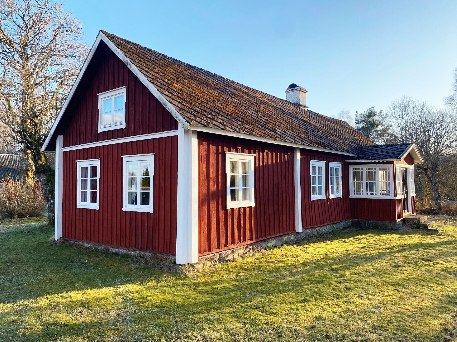 A red wooden house with white trim, a gabled roof, and a chimney.